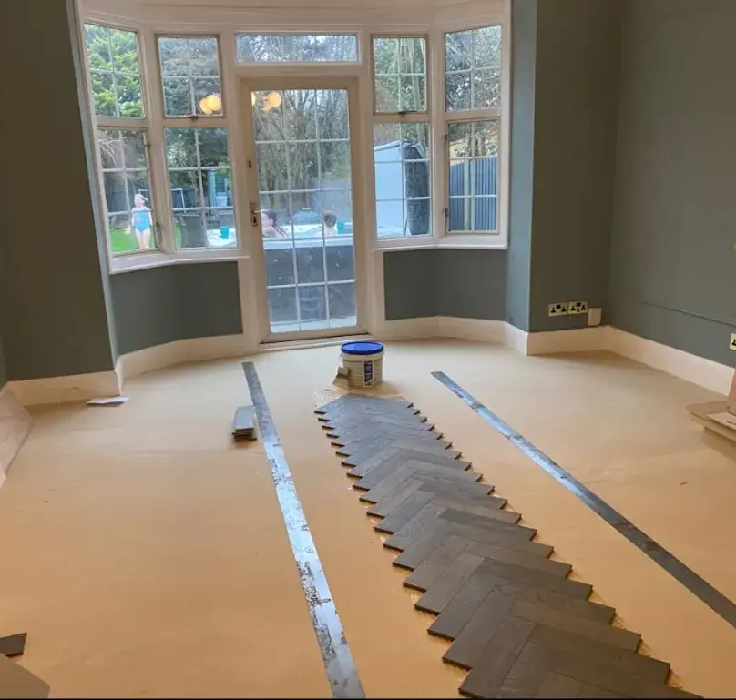 Room with partially laid herringbone wood floor, gray walls, and a bay window