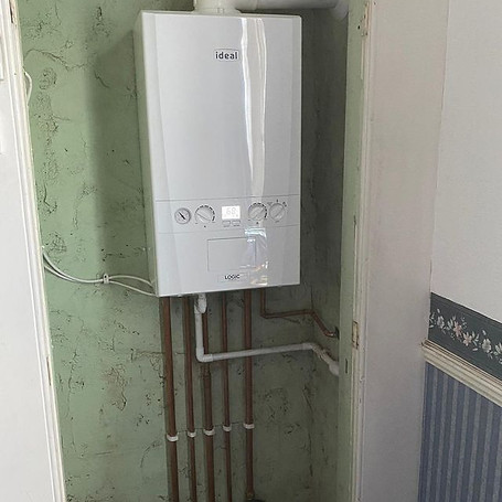 A white 'Ideal' boiler with copper pipes, installed in a green and striped cupboard