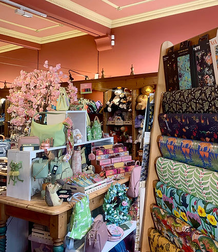 A cozy store interior with colorful fabrics rolled up, pink cherry blossoms, and shelves filled with bags and decorative items