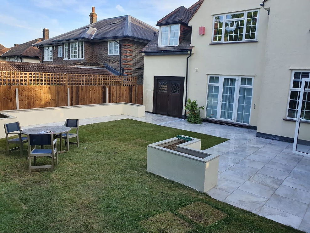 A modern backyard with a mix of grass and tiled patio, featuring a small table with four chairs, and a planter box