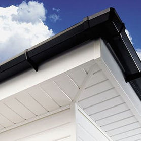 Close-up of a house roof corner featuring white soffit and fascia with black gutters