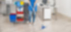 A person mops an office floor next to a cleaning cart with supplies