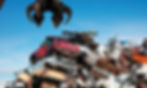 A claw crane hovers over a pile of scrapped cars and metal debris