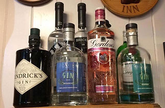 Bottles of various gin brands are displayed on a shelf, including Hendrick's, Gordon's, and others
