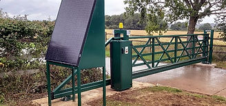 A solar-powered gate in a rural setting with a grassy field and trees in the background