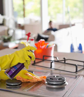 A person wearing yellow gloves sprays cleaner over a stovetop