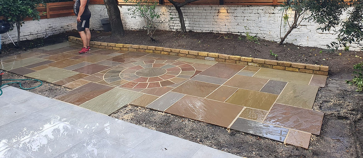 A man in athletic wear stands on a newly laid stone patio in a garden