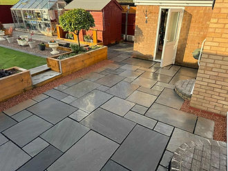 Modern backyard patio with large gray stone tiles, bordered by raised wooden planters and a small lawn