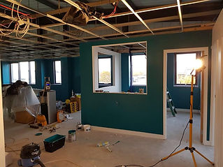 Under-construction office space with teal walls, exposed ceiling wires, and scattered tools