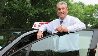 driving instructor leaning against a car with an 'L' plate on the roof
