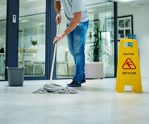 A person mops a shiny office floor near a yellow caution sign reading Caution Wet Floor