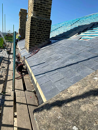 A slate roof under construction with neatly aligned tiles and a brick chimney