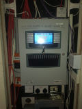 A digital control panel mounted on a wall, surrounded by red and white cables