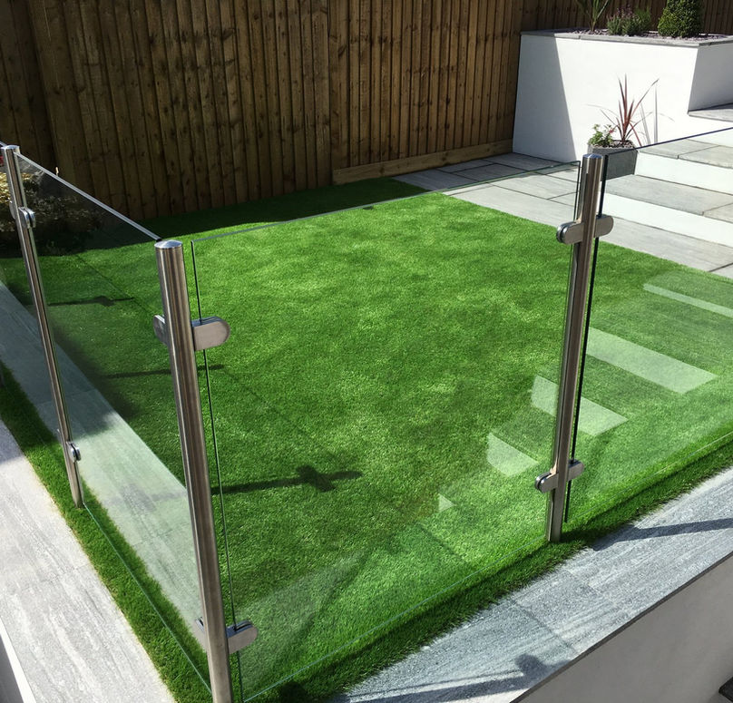 A small, fenced area of vibrant green artificial grass bordered by sleek glass panels