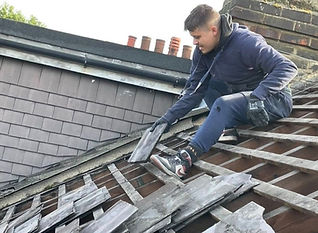 A roofer removing old broken slate tiles and exposing the wooden battens underneath