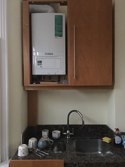 A modern Vaillant boiler is installed in a small wooden cupboard or airing cupboard