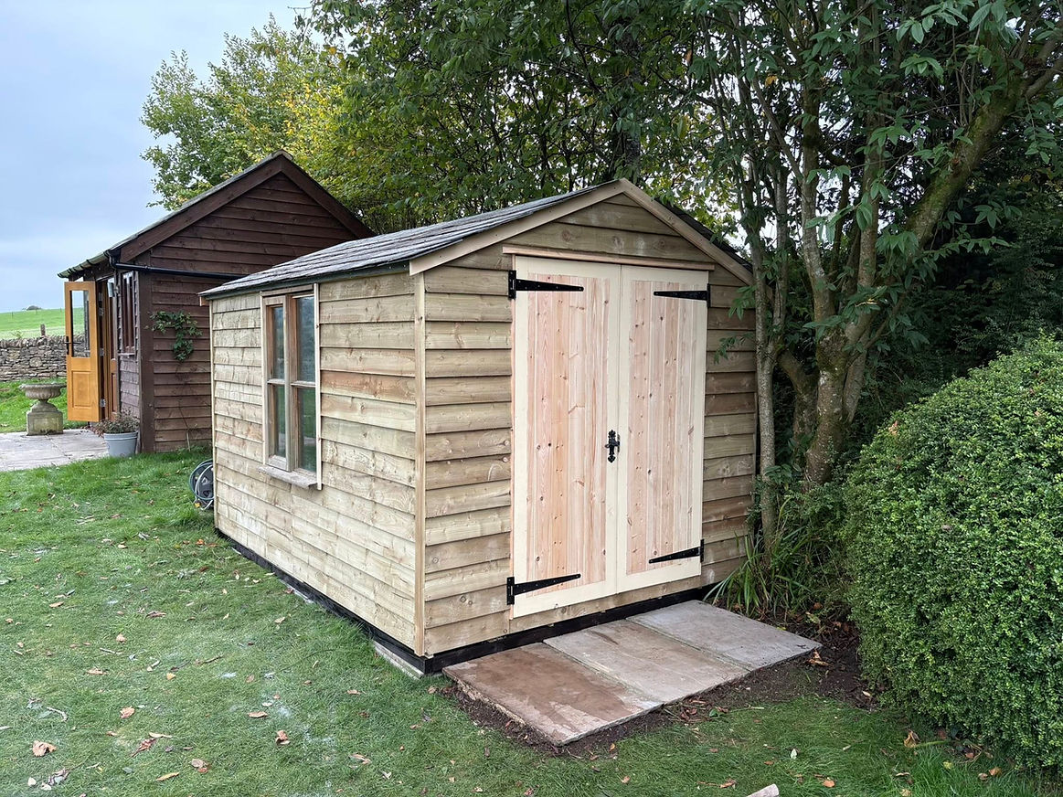 A small wooden shed with a sloped roof is set in a grassy garden