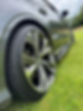 Close-up of a sleek car's alloy wheel with intricate spoke design, parked on green grass