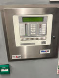 A wall-mounted metal fire alarm control panel with a digital display and keypad