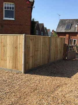 Wooden fence bordering a gravel driveway, adjacent to a brick house with a white-framed window