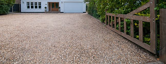 Wide view of a gravel driveway leading to a white garage door and wooden entrance