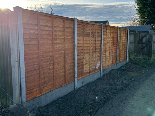 Wooden fence with vertical slats bordered by concrete posts runs along a narrow path