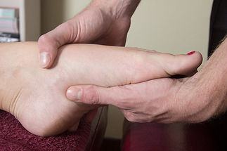 Hands gently massaging a foot on a maroon towel, suggesting a relaxing and therapeutic setting