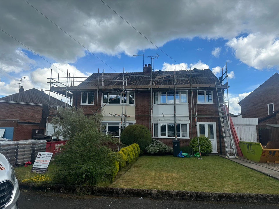 A two-story house with scaffolding for roof work under a partly cloudy sky