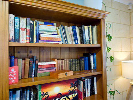 An image of a homely wooden bookcase taken at the Bruce Psychology clinic in Mandurah, featuring many books from philosophy to psychology, a lamp, and antique shelf ornaments.