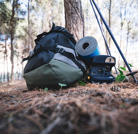 Backpacking gear including a hiking backpack, trekking poles, and camping equipment at a forest campsite.