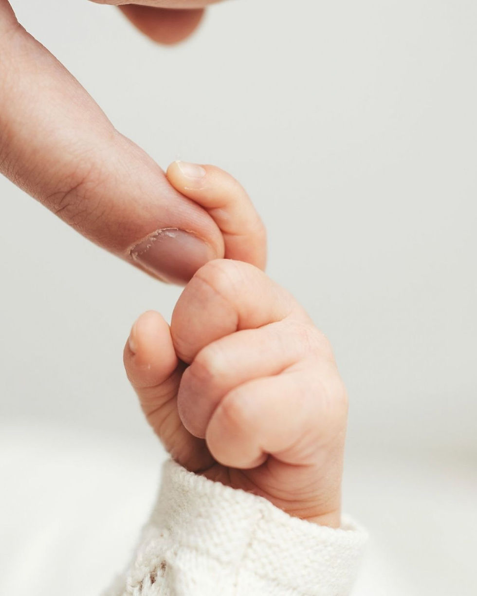 Close-up of a baby hand tightly holding an adult finger against a soft white background, showing a gentle bond