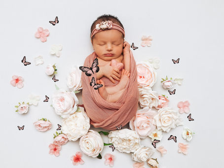 Newborn wrapped in pink, surrounded by roses and butterflies on white. Peaceful mood with pastel colors and floral details.