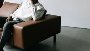 Personne assise sur un canapé en cuir, tête appuyée sur la main, dans une pièce minimaliste. L’image suggère un moment de pause, de réflexion ou d’introspection, en lien avec le ralentissement et la santé mentale.