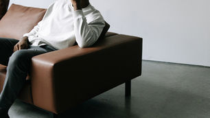 Personne assise sur un canapé en cuir, tête appuyée sur la main, dans une pièce minimaliste. L’image suggère un moment de pause, de réflexion ou d’introspection, en lien avec le ralentissement et la santé mentale.