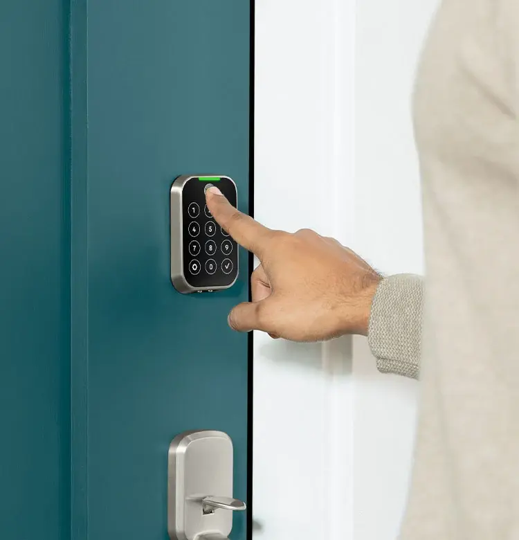 Hand pressing a digital keypad on a teal door beside a silver lock, suggesting entry into a home.