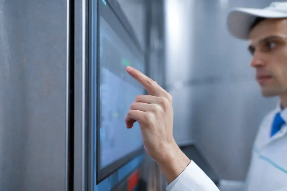 Manufacturing technician configuring electromechanical assembly system on industrial touchscreen interface in cleanroom facility