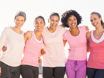 Five women in activewear, smiling and embracing outdoors against a clear sky. They wear shades of pink and look joyful and supportive. Focusing on women's health and hormone health