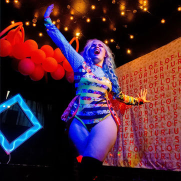 drag performer lip syncing on stage with flourish backdrop