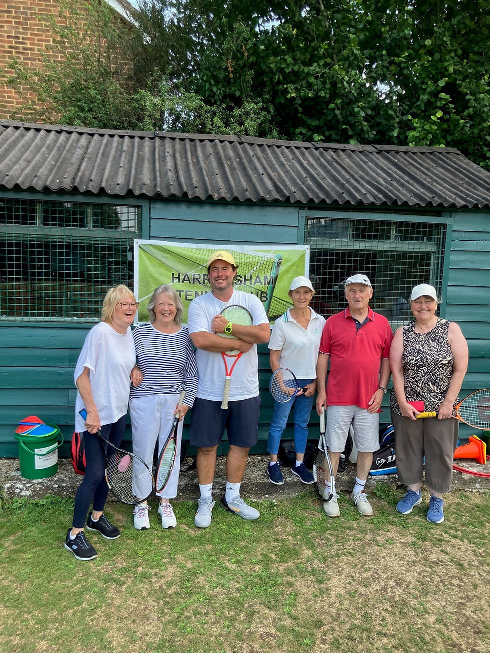Six smiling walking tennis players pose with rackets outside a teal clubhouse beneath a green TENNIS CLUB banner.