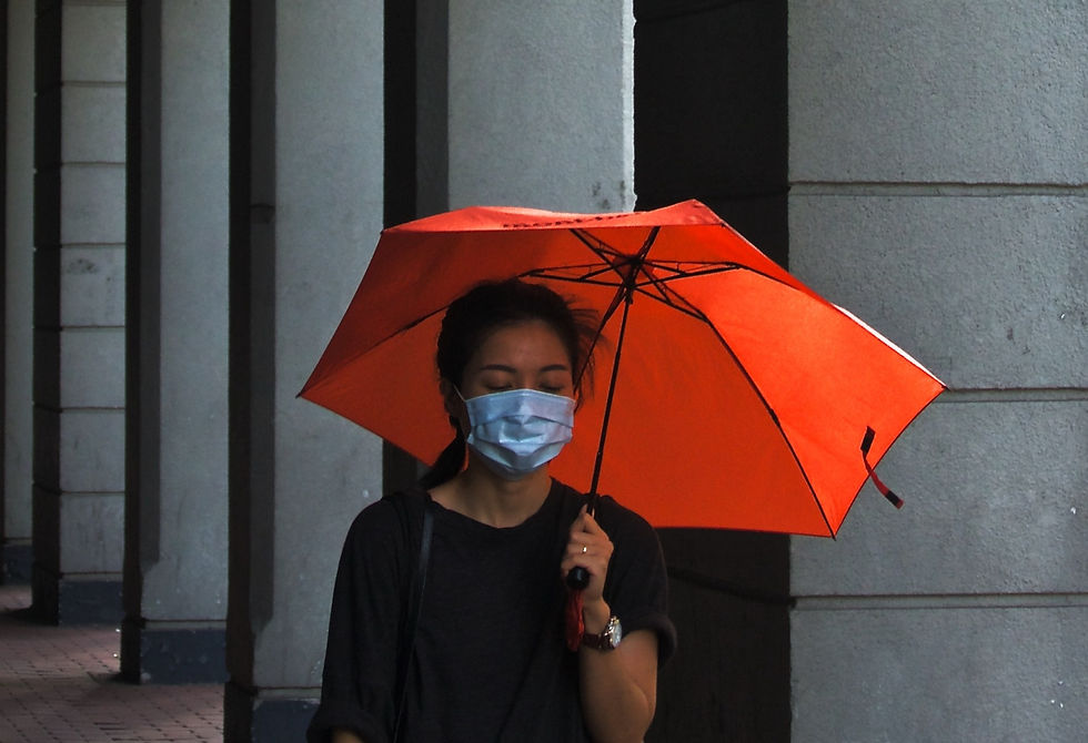Mulher asiática andando na rua, olhando para baixo, segurando um guarda chuva laranja e usando mascara
