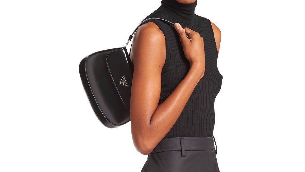 Vemos apenas o tronco de uma modelo negra, usando regata preta de gola alta e segurando uma bolsa no ombro, também preta e com símbolo da Prada