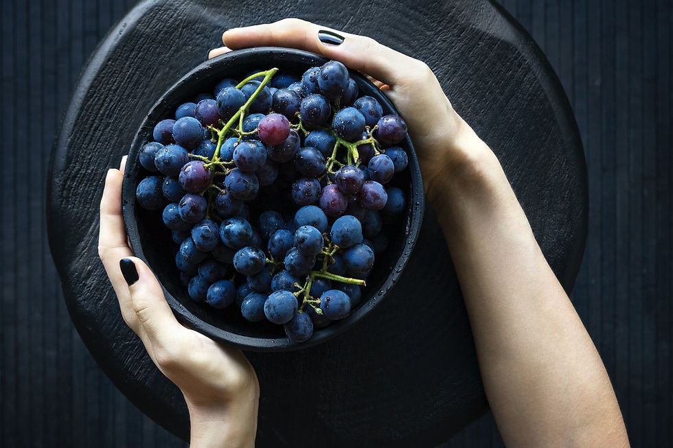 bowl com um cacho de uvas roxas, visto de cima. um par de mãos segura o bowl pelos dois lados
