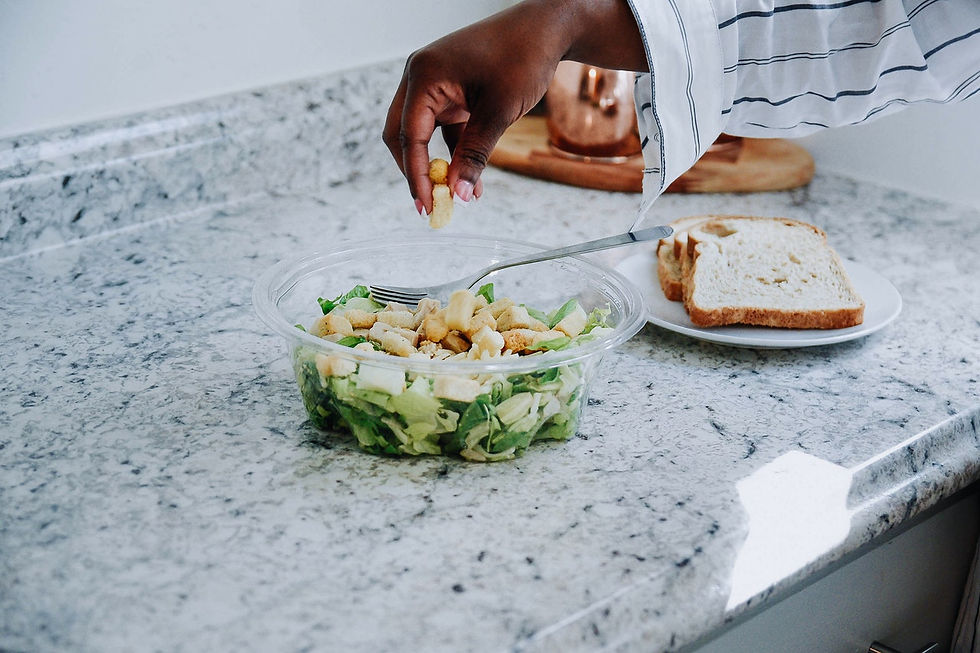Foto de uma bancada de cozinha com um pote de salada sendo temperado pela mão de uma pessoa preta