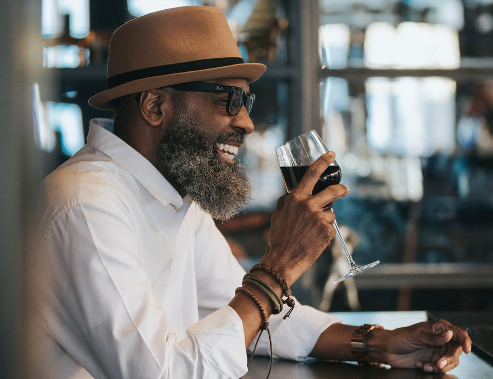 Homem negro de perfil, sorrindo e segurando uma taça de vinho na mão