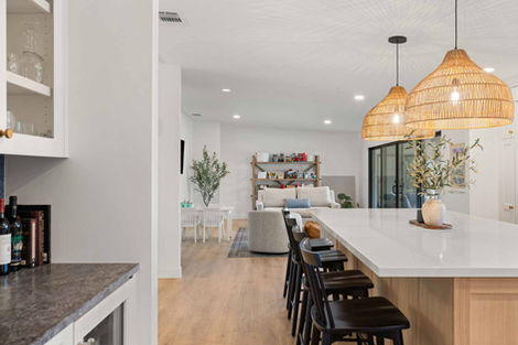 Kitchen counter and bar stools with view into open-concept living room designed by H&H Builds.