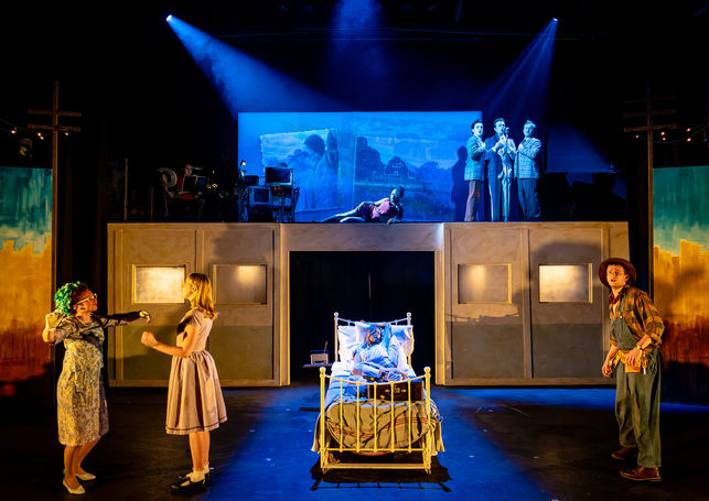 A wide shot of the stage, a bed in the middle with enesemble members singing and dancing around it