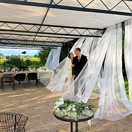 Newlyweds beneath the draped wedding pergola at Stacija Suntaži