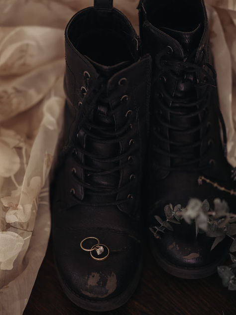 Black boots paired with a wedding dress, symbolizing a New England elopement adventure, with rings on top and a blurred bouquet.