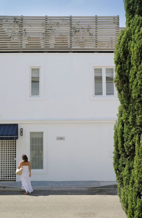 Woman in white dress by a white building and tall green tree