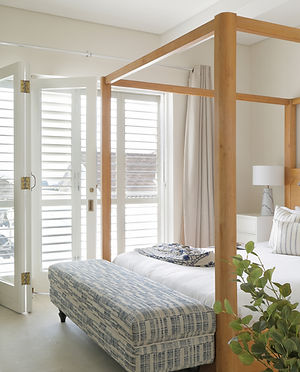 Modern bedroom with wooden four-poster bed and white shutters
